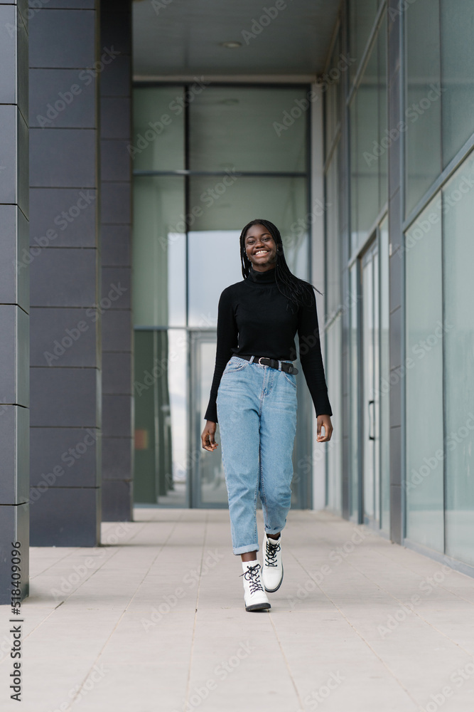 Cheerful black woman walking outside modern building Cheerful black woman walking outside modern building