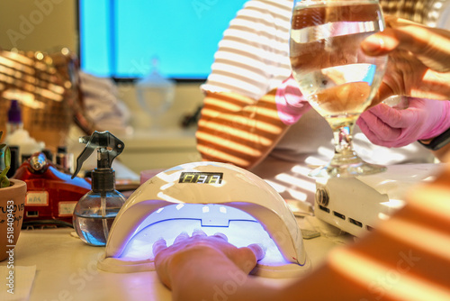 Woman drinks water while drying gel nail polish in a lamp in a salon  photo