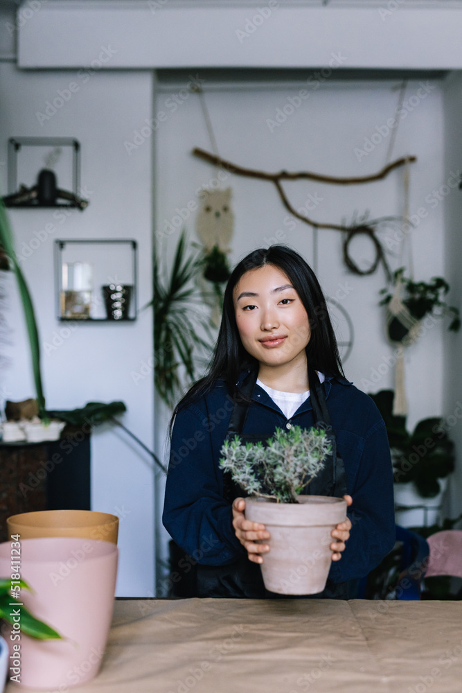 Asian seller with potted plant in contemporary floral shop Asian seller with potted plant in contemporary floral shop