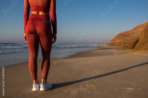 Woman at the sportive clothes standing at the sandy beach near the ocean