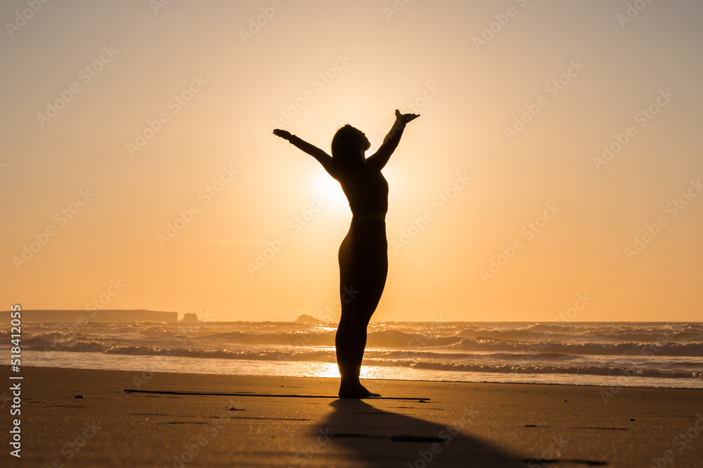 Woman doing yoga pose and greeting to sun on the seashore at sunset