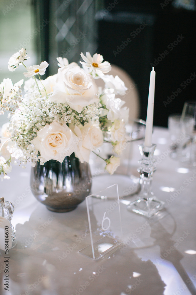 Wedding decor of a banquet table of snow-white color. White roses, peonies, gypsophila, white candles in glass candlesticks. Wedding decor of a banquet table of snow-white color. White roses, peonies, gypsophila, white candles in glass candlesticks.