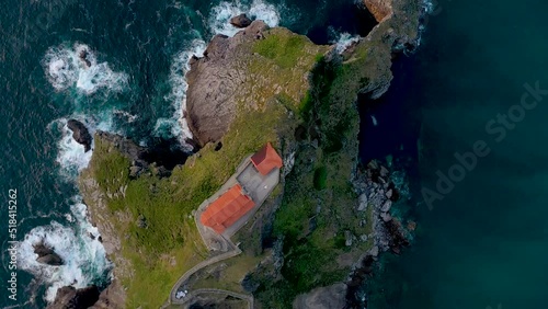 Drone rotating above the Gaztelugatxe Isle. View of San Juan de Gaztelugatxe, an hermitage dedicated to John the Baptist. Waves splashing on the rocks. Warms colours reflecting on building and water