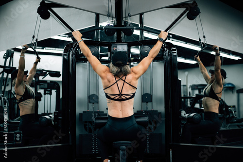 Muscular woman using machine at gym wearing black workout clothi