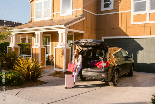 Latina using phone by SUV car and suitcase in sunny townhouse photo