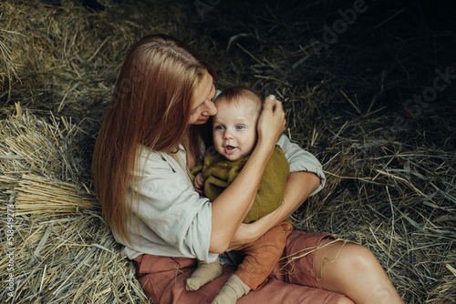  Mother tightly hugs her little son sitting in the hayloft