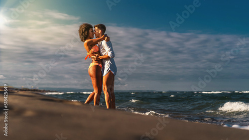 Multiracial heterosexual couple kissing and hugging on the beach - Multiethnic newlyweds in honeymoon kissing on the beach