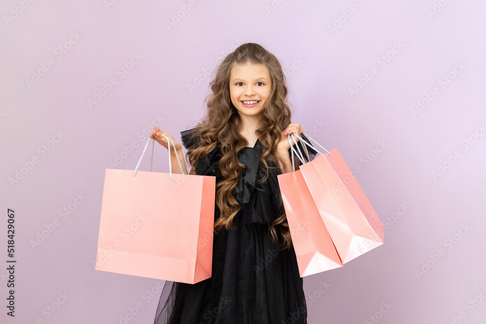 A child holds paper shopping bags. A beautiful little girl with curly hair is holding on a pink isolated background. A child holds paper shopping bags. A beautiful little girl with curly hair is holding on a pink isolated background.