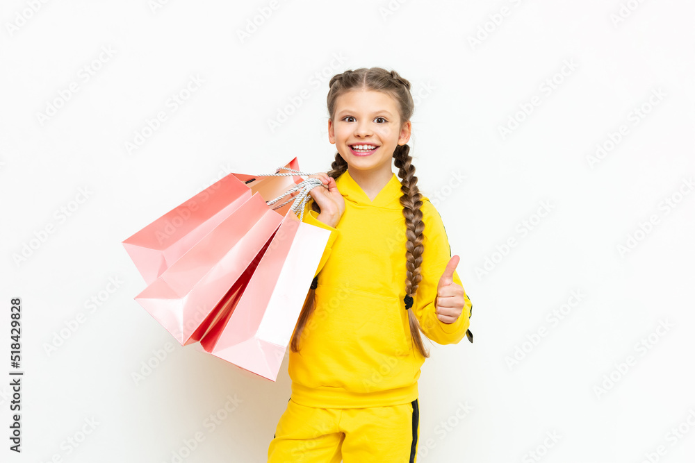 Shopping for children. A beautiful little girl in a yellow sports suit holds paper shopping bags on a white isolated background. Shopping for children. A beautiful little girl in a yellow sports suit holds paper shopping bags on a white isolated background.