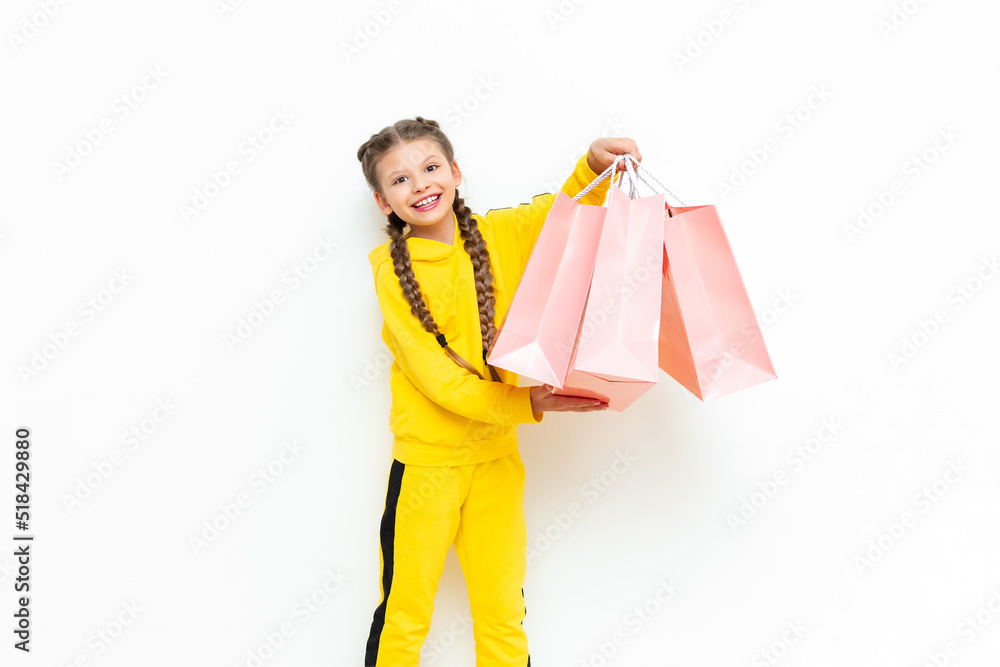 The child is happy with new purchases. Shopping for children. A beautiful little girl in a yellow tracksuit holds paper bags. The child is happy with new purchases. Shopping for children. A beautiful little girl in a yellow tracksuit holds paper bags.