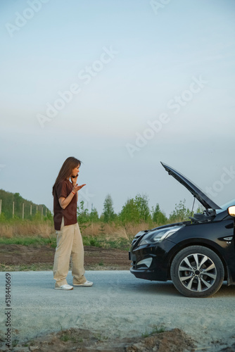 Puzzled woman talking on smartphone near broken car photo