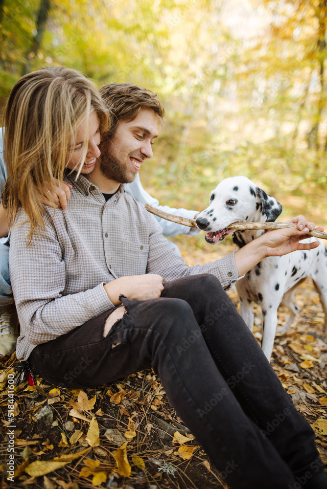 Happy couple playing with wooden stick with dog Happy couple playing with wooden stick with dog