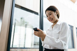 Asian businesswoman in formal suit in office happy and cheerful during using smartphone and working.