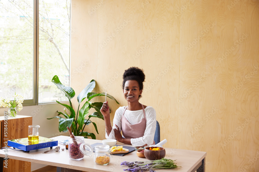 Merry black woman at table with cosmetic ingredients
