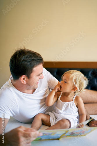 Smiling dad reading colorful book to little girl