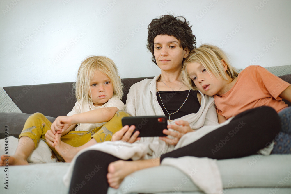 Two boys and an adult woman are watching cartoons on a smartphone. Two boys and an adult woman are watching cartoons on a smartphone.