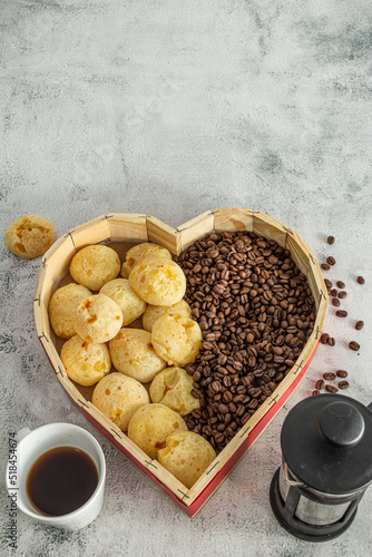 brazilian cheese bread or 'pão de queijo' in a heart shaped format basket, with coffee beans on a marble or stone surface photo