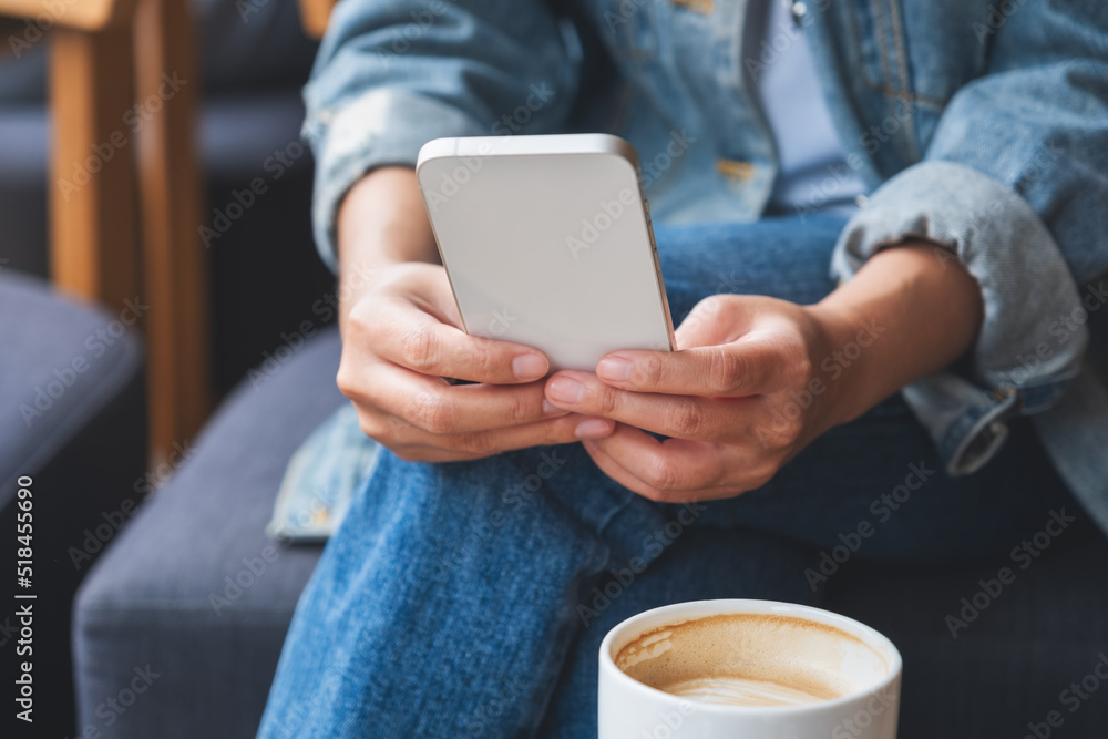 Closeup image of a woman holding and using mobile phone with coffee cup on the table Closeup image of a woman holding and using mobile phone with coffee cup on the table
