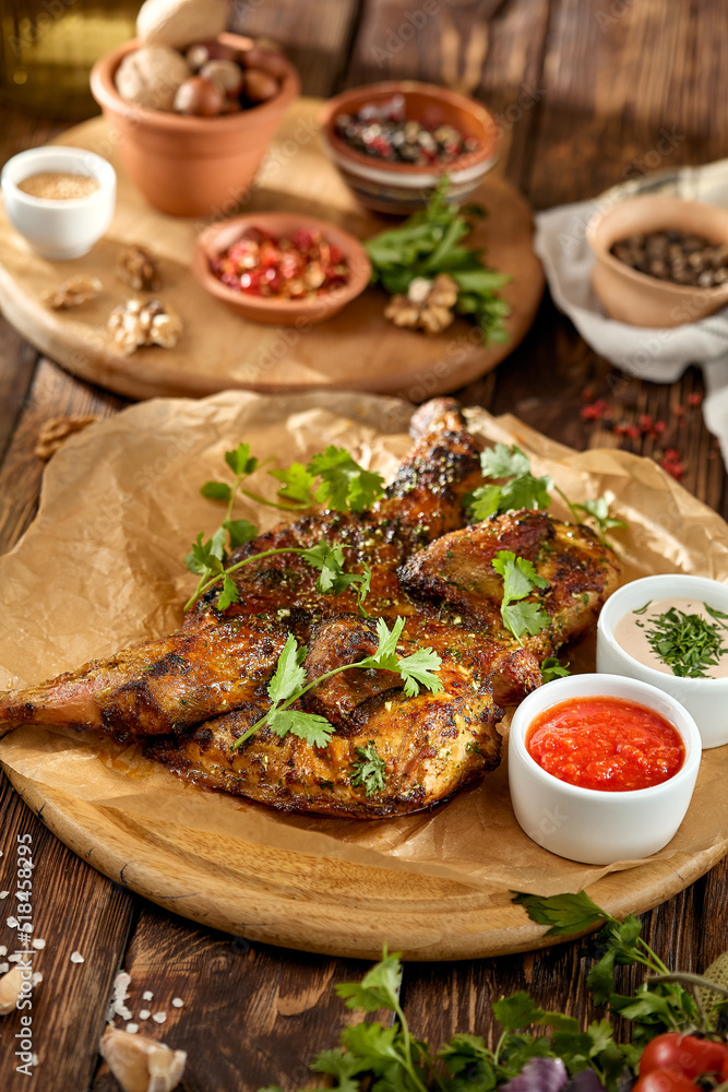 Traditional georgian dish - chicken tabaka on wooden background in rustic style. Roasted whole chicken in georgian style on wooden table. Chicken tabaka with sauces in rustic style. Traditional georgian dish - chicken tabaka on wooden background in rustic style. Roasted whole chicken in georgian style on wooden table. Chicken tabaka with sauces in rustic style.