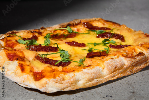 Italian pizza with cheese and dried tomatoes on dark background. Cheese pinsa on gray stone table with hard shadow. Roman pizza with cheese and tomatoes on concrete background. Pinsa menu.