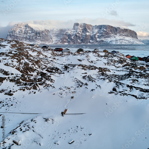 Mushing Greenlandic dog sled up hill in Uummannaq, midwinter photo