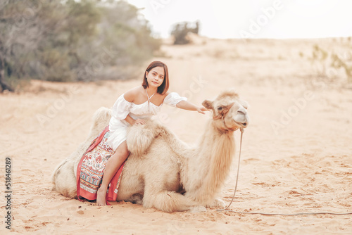 Portrait of asian young woman tourist in white dress and landscape with tourists riding on camels is popular travel destination in Mui Ne desert, Vietnam