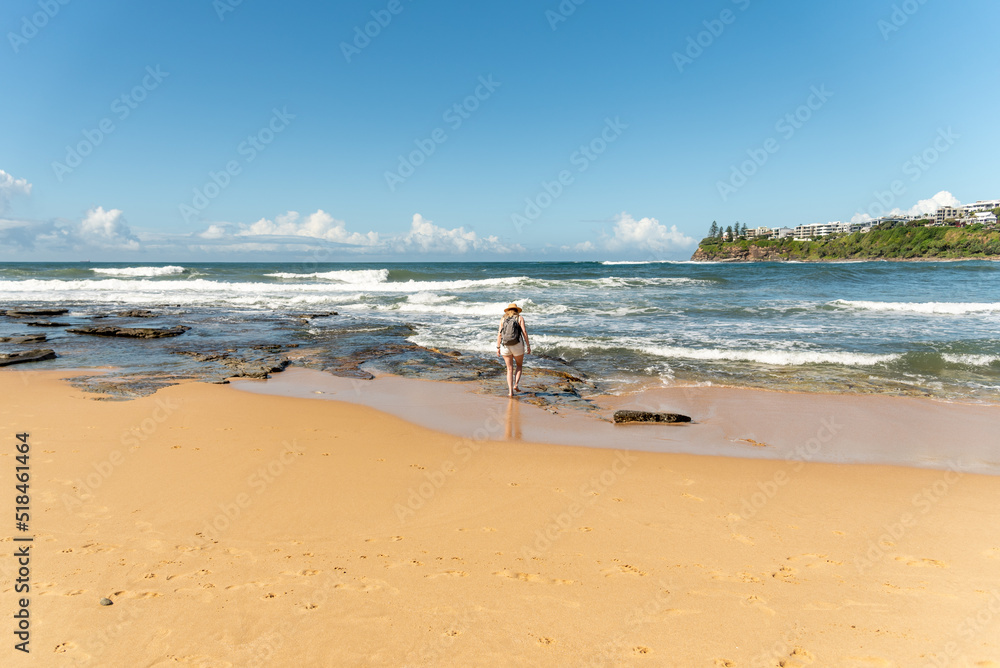 Woman walking along scenic beach view in summer time on blue sky day. 
