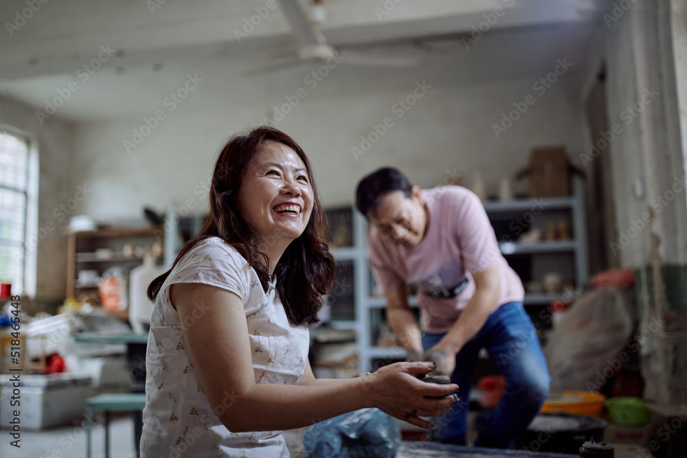 East Asian Small Business Owner Laughs While In Her Pottery Workshop East Asian Small Business Owner Laughs While In Her Pottery Workshop