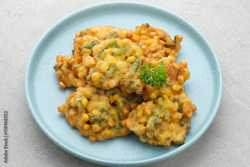 Perkedel Jagung or Bakwan Jagung, corn fritters is Indonesian traditional food. Savoury snack made of corn, egg, flour, spring onion, pepper and salt. Served in plate on grey background.
