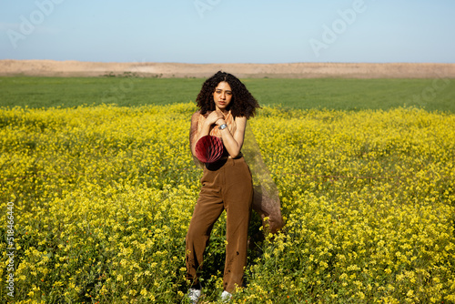 Young girl with curly hair posing in a flowers field holding accessory photo