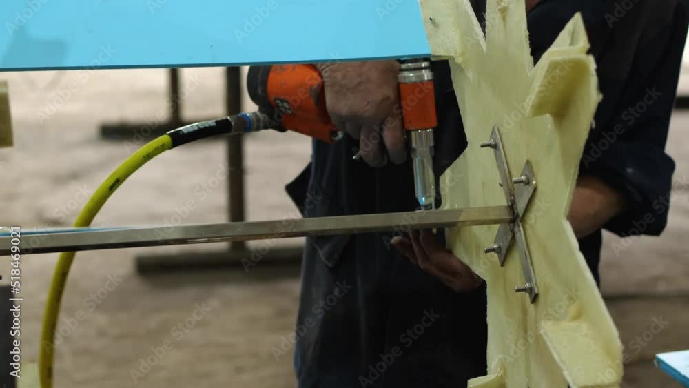 Close-up of a male mechanic working with a pneumatic tool with a riveting gun. A worker in a private shop assembling pedal-powered catamarans. Fixing propeller blades Close-up of a male mechanic working with a pneumatic tool with a riveting gun. A worker in a private shop assembling pedal-powered catamarans. Fixing propeller blades