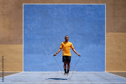 Fit black sprinter jumping in stadium on sunny day