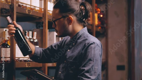 Young Asian sommelier is checking the drink store. A bartender wearing glasses and hair tie Wine stands to check the drink list and prepares to serve drinks to customers at the hotel bar. photo