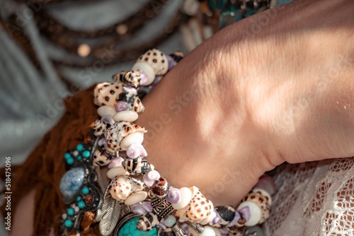 Close up of beautiful tribal boho style woman hands with lots of accessories. Boho style for fashionable look on resort. Middle aged well looking woman in white dress and boho style braclets.