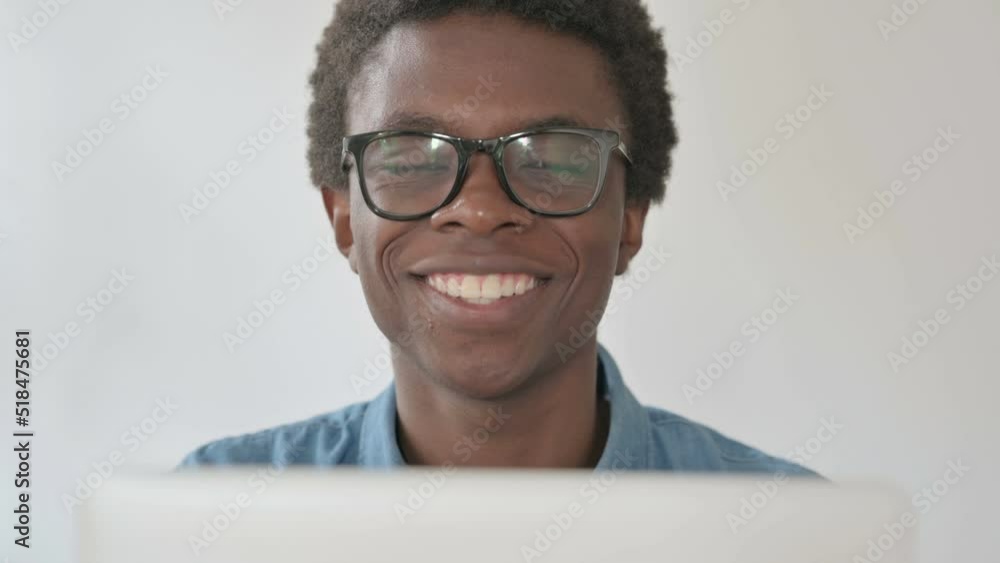 Close Up of Young African Man Smiling at Camera while using Laptop in Office Close Up of Young African Man Smiling at Camera while using Laptop in Office