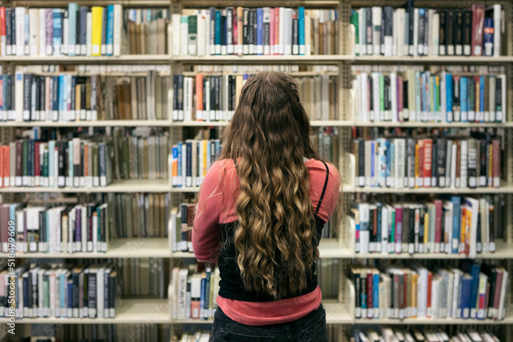 Student Looking At Bookshelves In Library Student Looking At Bookshelves In Library