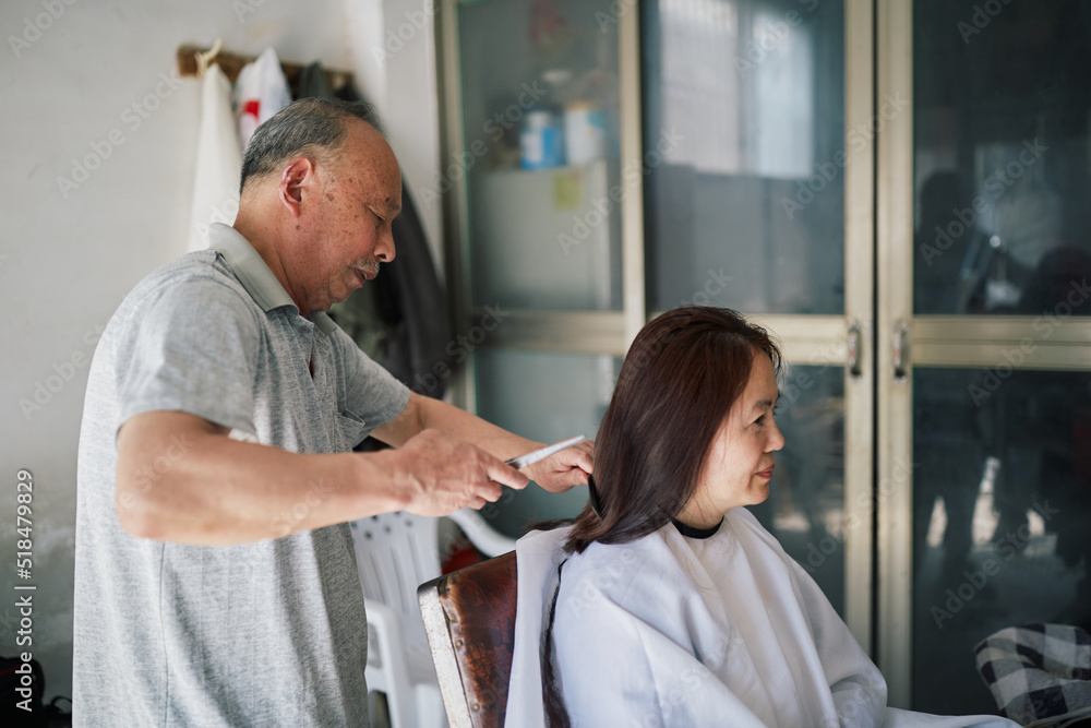 Older Asian Hairstylist Cuts A Customer's Hair At His Salon. Older Asian Hairstylist Cuts A Customer's Hair At His Salon.
