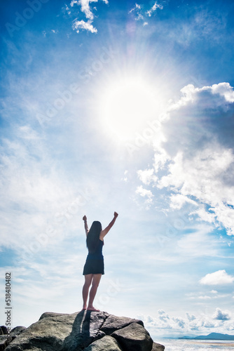 Rear view of woman standing on rock with arms raised against blue sky