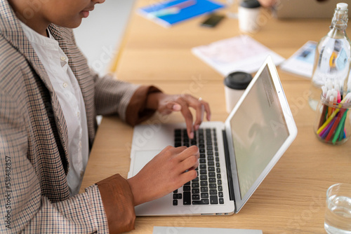 Crop black woman writing article on laptop