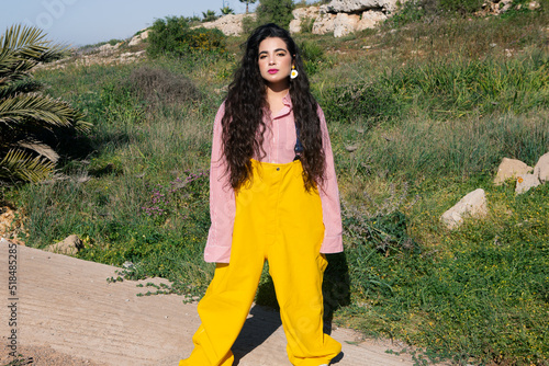 Young girl with long black curly hair wearing yellow jumsuit in nature photo