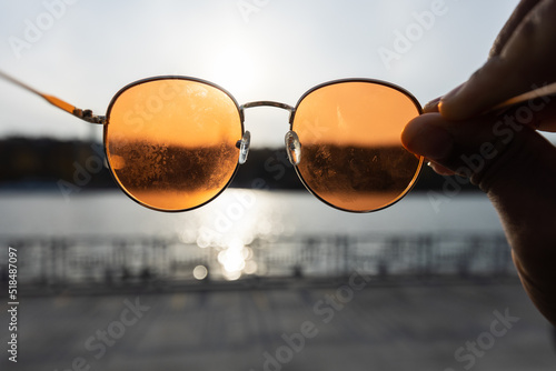 Orange sun glasses hold in front of the direct sun with view to river  photo