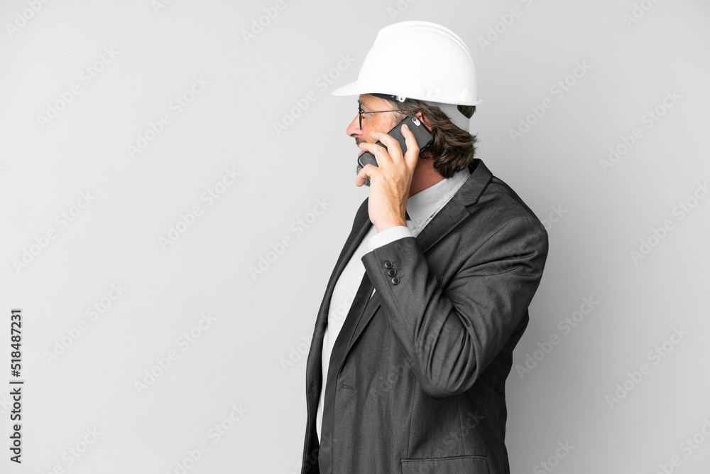 Young architect man with helmet over isolated background keeping a conversation with the mobile phone with someone Young architect man with helmet over isolated background keeping a conversation with the mobile phone with someone