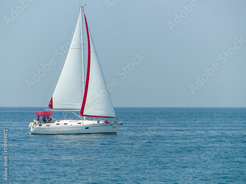 A white boat with a white sail floats on a calm blue sea
