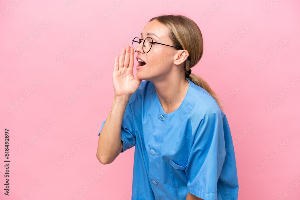 Young nurse doctor woman isolated on pink background shouting with mouth wide open to the lateral Young nurse doctor woman isolated on pink background shouting with mouth wide open to the lateral
