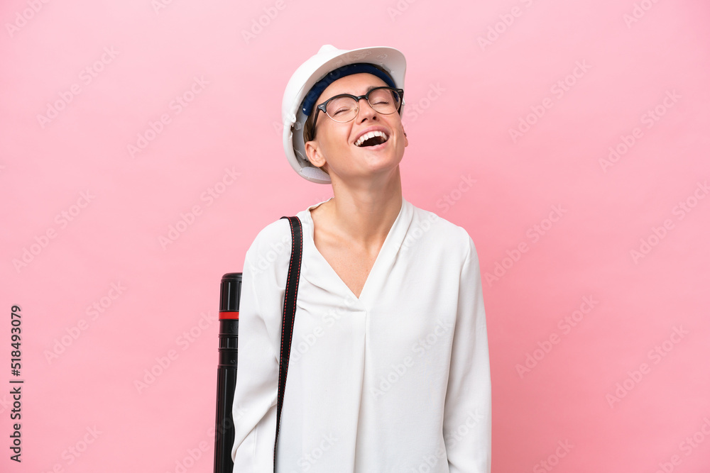 Young architect Russian woman with helmet and holding blueprints isolated on pink background laughing Young architect Russian woman with helmet and holding blueprints isolated on pink background laughing