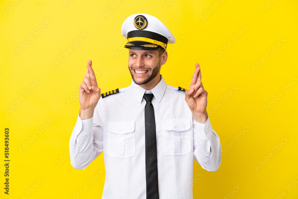 Airplane caucasian pilot isolated on yellow background with fingers crossing Airplane caucasian pilot isolated on yellow background with fingers crossing