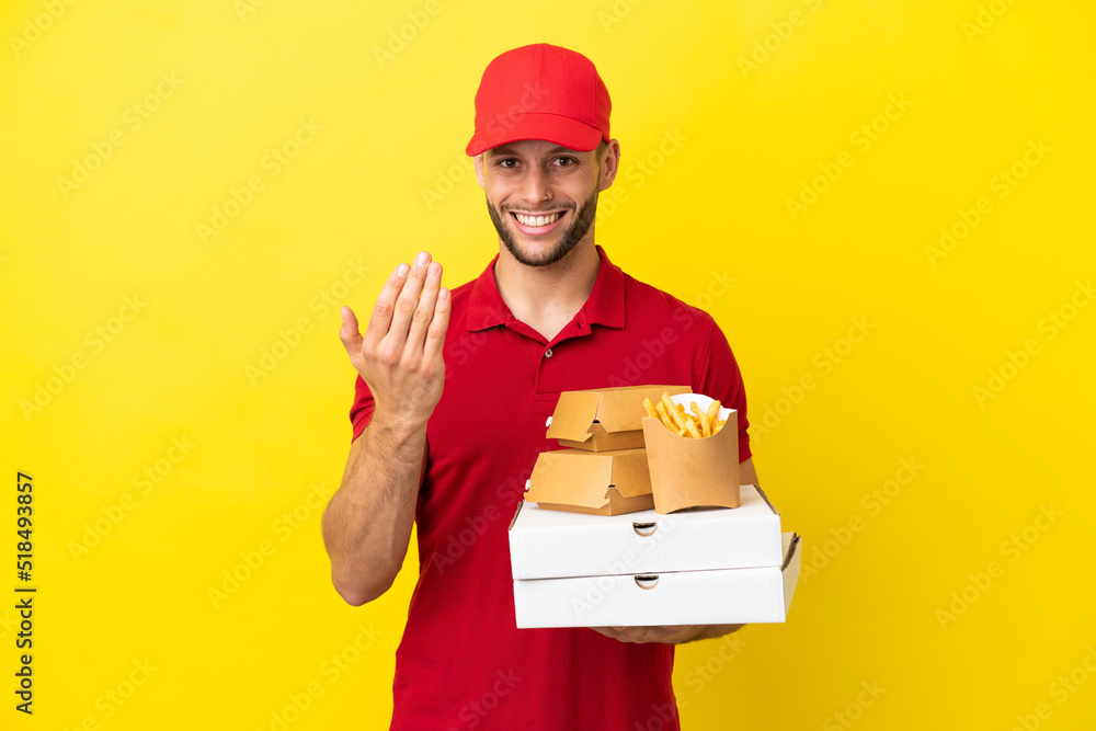 pizza delivery man picking up pizza boxes and burgers over isolated background inviting to come with hand. Happy that you came pizza delivery man picking up pizza boxes and burgers over isolated background inviting to come with hand. Happy that you came