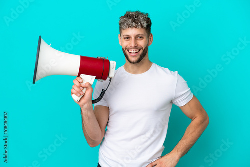 Young handsome caucasian man isolated on blue background holding a megaphone and smiling