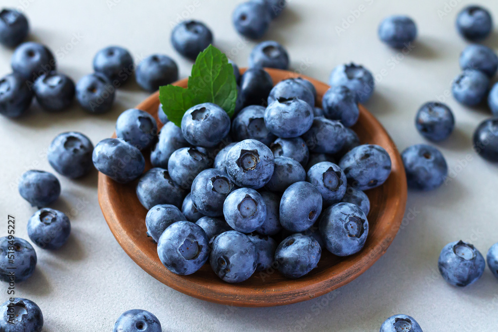 Bowl of fresh ripe blueberries with leaves on kitchen table Bowl of fresh ripe blueberries with leaves on kitchen table