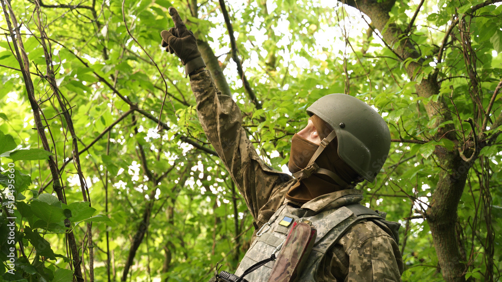 Ukrainian soldier hides from an air attack in the forest. shelling. mortar shelling, aircraft attack on infantry positions. a soldier watches the sky in a forest shelter and points to a threat